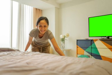 Neşeli ve mutlu bir kadın yeşil ekran televizyonu olan rahat bir yatak odasını düzenliyor.