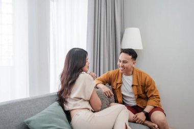 İki yakın arkadaş, şık ve rahat bir yaşam alanında hareketli bir şekilde sohbet ediyorlar.