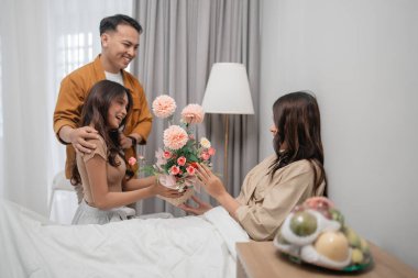 Neşeli bir sahnede bir çift, sevgi dolu sıcak bir odada bir kadına çiçek veriyor.