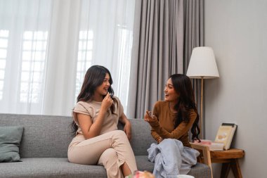 İki yakın arkadaş, sıcak bir oturma odasında birlikte gülüp sohbet ediyorlar.