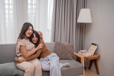 İki arkadaş rahat bir kanepede dinlenirken neşeli bir kahkahayı paylaşırlar..