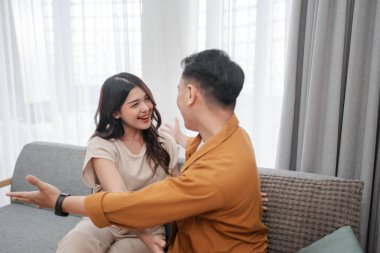 Neşeli bir çift, samimi ve davetkar bir oturma odasında birlikte kahkaha ve sıcaklık paylaşıyor.