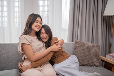 İki güler yüzlü arkadaş birbirlerini kucaklarken rahat bir kanepede dinlenirler.