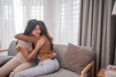 Sıcak bir oturma odasında, iki neşeli kadın sevgi ve rahatlık dolu sıcak bir kucaklaşmayı paylaşıyor.