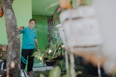 Çalışkan bir adam yemyeşil çimlerle çevrili canlı bir bahçede çeşitli bitkilerle ilgilenir.