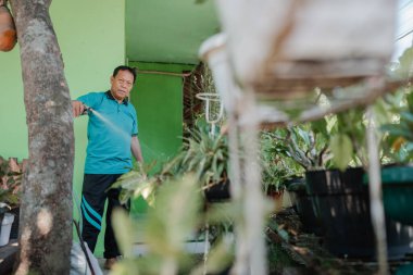 Bir adam neşe içinde bahçesini renklerle dolu canlı bir ortamda sular.