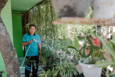 Canlı bahçesiyle ilgilenen bir adam bol yeşillik ve çiçek açan bitkiler sergiliyor.