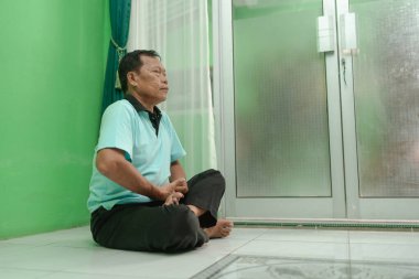 Bir adam huzur içinde, yumuşak, doğal ışıkla dolu yeşil bir odada meditasyon yapıyor.