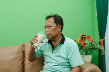 Sıcak bir oturma odasında ferahlatıcı bir içki içen bir adam, yeşil bir arka planla havayı güçlendirir.