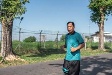 Yeşillik ve ağaçlarla çevrili güzel manzaralı bir yolda koşan bir adam.