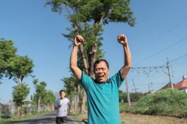 Güneşli güzel bir günde, iki adam neşeli bir şekilde birlikte koşar, çevrende canlı yeşillik ve doğa vardır.