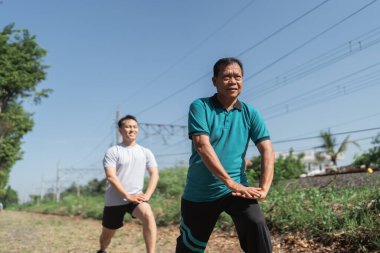 Erkekler sıcak ve güneşli bir günde dışarıda esneme hareketleri yapıyorlar, sağlık ve sağlığa odaklanıyorlar.