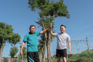 İki yakın arkadaş neşeli bir şekilde doğa güzelliğiyle çevrili açık havada beşlik çakar.