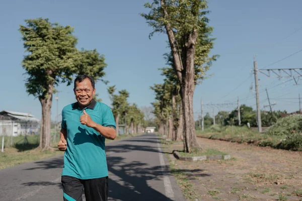 Neşeli bir adam ağaçlı bir patika boyunca güzel bir sabah ışığında enerjik bir şekilde koşuyor.