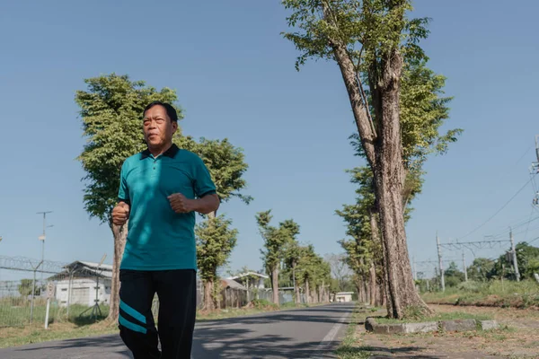Açık mavi gökyüzünün altında yemyeşil ağaçlarla çevrili manzaralı bir yolda koşan bir adam.