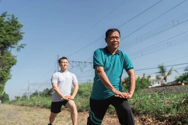 Erkekler sıcak ve güneşli bir günde dışarıda esneme hareketleri yapıyorlar, sağlık ve sağlığa odaklanıyorlar.
