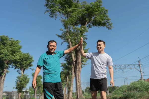 İki yakın arkadaş neşeli bir şekilde doğa güzelliğiyle çevrili açık havada beşlik çakar.