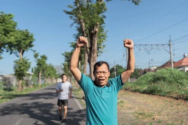 İki adam keyifli bir şekilde birlikte koşuyorlar, açık mavi gökyüzünün altında zindeliklerini kutluyorlar.