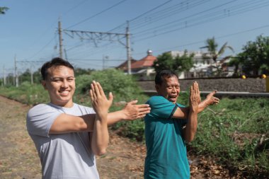 Erkekler güneşli bir ortamda mutlu bir şekilde esneyerek ve egzersiz yaparak temiz havanın tadını çıkarıyorlar.
