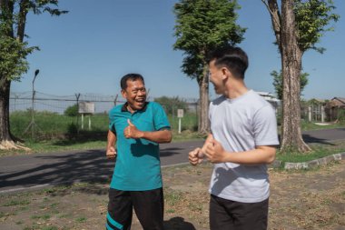 Canlı, güneşli yeşil bir park ortamında birlikte koşan ve gülen iki adam.