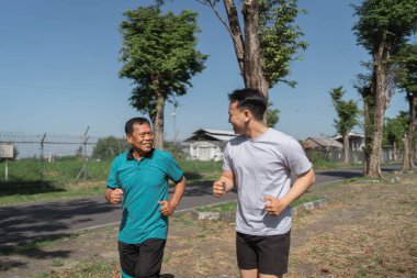 Güneşli bir parkta birlikte koşan bir grup arkadaş hem spor hem de arkadaşlığı destekliyor.