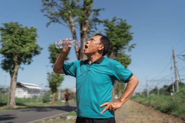 Bir adam dışarıda dinleniyor. İyi bir antrenmandan sonra biraz suyun tadını çıkarıyor.