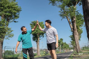 Arkadaşlar spor başarılarını güneşli ve enerjik bir parkta beşlik çakarak kutluyorlar.