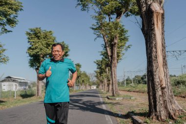 Neşeli bir koşucu, doğanın canlı yeşilliğinde ferahlatıcı bir sabah koşusunun tadını çıkarıyor.