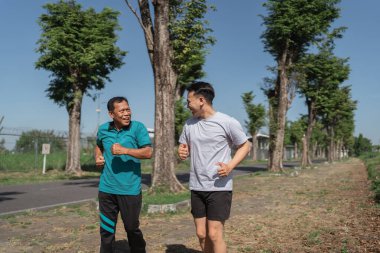 İki mutlu adam, bereketli ağaçlar ve hayat dolu bir parkta birlikte koşuyor.