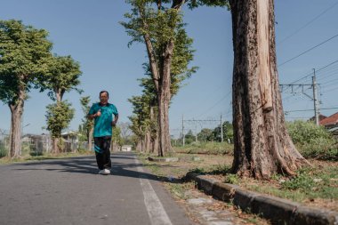 Bir adam, güzel ağaçlarla çevrili sakin bir yolda çok huzurlu bir şekilde koşar.