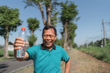 Neşeli bir adam, kırsal bir yolda güneşli bir günde parlak bir su şişesi sergiliyor.