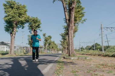 Genç bir insan, ağaçlar ve doğa ile çevrili ıssız bir yolda huzur içinde koşar.