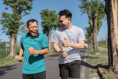 İki erkek mutlu bir şekilde birlikte koşuyor, gülümsüyor ve dışarıda eğlenceli, sağlıklı bir aktivitenin tadını çıkarıyor.