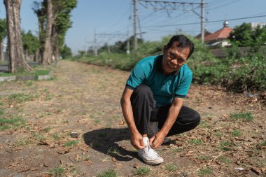 Bir adam, dışarıda huzurlu bir ortamın tadını çıkarırken bağcıklarını bağlamak için diz çöküyor.
