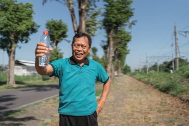 Enerjik bir adam, açık hava egzersizinden sonra gülümserken kendine güvenen bir su şişesi tutar.