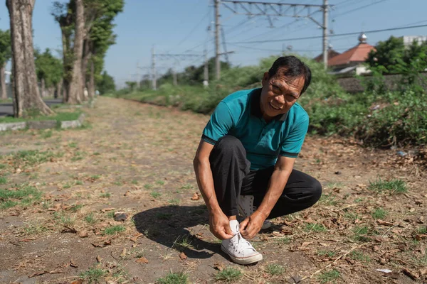 Bir adam, dışarıda huzurlu bir ortamın tadını çıkarırken bağcıklarını bağlamak için diz çöküyor.