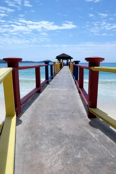 Colorful concrete and wooden jetty jutting out over a clear blue calm sea, the sky is blue with white fluffy clouds, the sun is shining a typical tropical beach