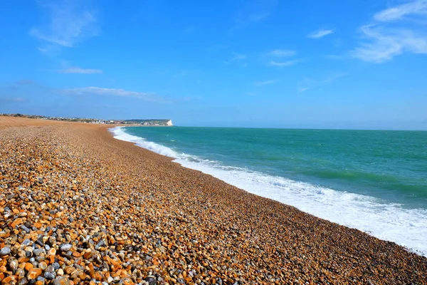 阳光明媚的一天锡福德海滩东苏塞克斯英国的长扫曲线在前景是鹅卵石海滩然后白色的打破波和平静的蓝色海和天空背后的距离是镇和粉笔悬崖的边缘 — 图库照片