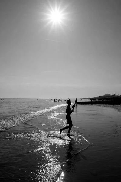 布莱顿海滩在一个炽热的阳光明媚的日子里 大海在阳光下闪闪发光 一个10岁的男孩在 Silhoutted 的时候被太阳晒到了海里 — 图库照片