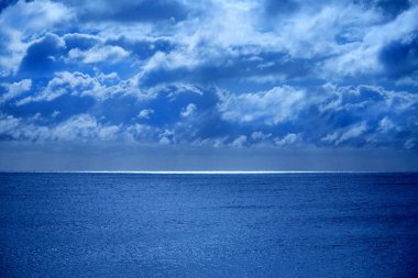 Deniz ve gökyüzü altındaki yarı sakin masmavi deniz, ufukta bir çizgi üst yarısında Moon pırıl pırıl parlayan ışık beyaz bulutlar içinde kabarık kaplı gökyüzü görüntü mavi parlaklık mehtap dan olmasıdır