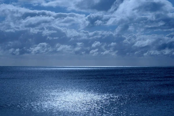 Deniz ve gökyüzü altındaki yarı sakin masmavi deniz, ufukta bir çizgi üst yarısında Moon pırıl pırıl parlayan ışık beyaz bulutlar içinde kabarık kaplı gökyüzü görüntü mavi parlaklık mehtap dan olmasıdır