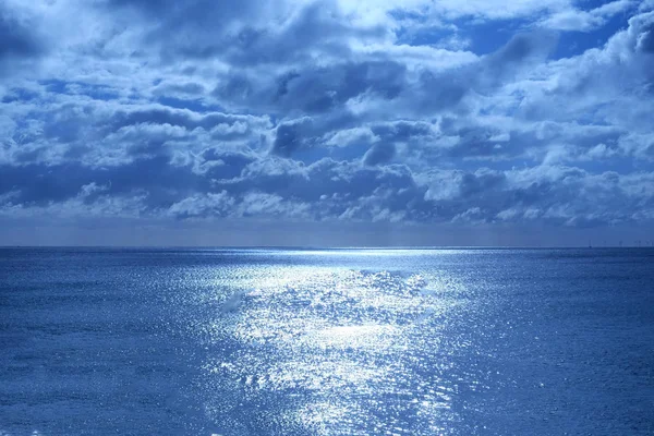 海和天空的下半部分是平静的深蓝色的大海 地平线上是一条白色的发光光芒 从月亮上半部分是天空中蓬松的云覆盖着月光下的蓝色光芒 — 图库照片