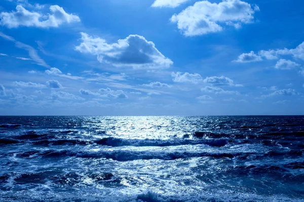 大海和天空 在下半部分是一个深蓝色的大海 海浪破浪 地平线上是一条白色的发光光芒 在水面上的上半部分是天空中蓬松的云 — 图库照片