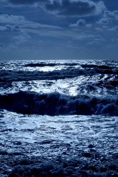 Şişme deniz dalgaları ile koyu mavi deniz karanlık gölgeler vardır burada dalgalar şişme ve güneş ışığı parlak beyaz ön planda ufukta denizin üzerinde olduğu bir karanlık Çakıl Plajı, dikey format üst yarısında gökyüzü kaplıdır