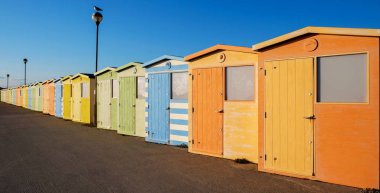 Yirmi parlak renkli plaj kulübe bir dizi yakın bir satır vardır renkli giderek azalan bir bakış açısı büyük turuncu, yeşil sarı arkalarında mavi mavi, orada iki sokak lambaları yakın bir satırda bir martı sit vardır