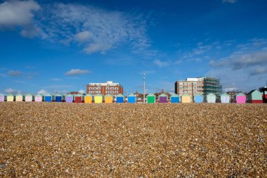 Ön planda bir yirmi üç renkli plaj kulübe hattıyız üstlerindeki merkezinde bir çakıl plajı beyaz bulutlar güneş parlıyor, Brighton, Sussex, veliahta, United İngiltere'de büyük bir mavi gökyüzü olduğunu