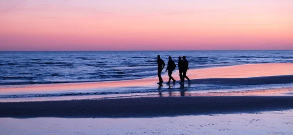 四个无法辨认的年轻人在阳光下走在荒芜的海滩上 — 图库照片
