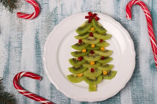 Kivi, mısır ve nar ağacından yapılmış Noel ağacı, Noel ve yeni yıl şenlik yemekleri için yaratıcı fikir, çocuklar için meyve atıştırmalığı