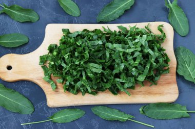 Karanlık bir arka plan üzerinde bulunan bir ahşap tahtada kuzukulağı dilimlenmiş kontur üzerinde kuzukulağı yaprakları vardır