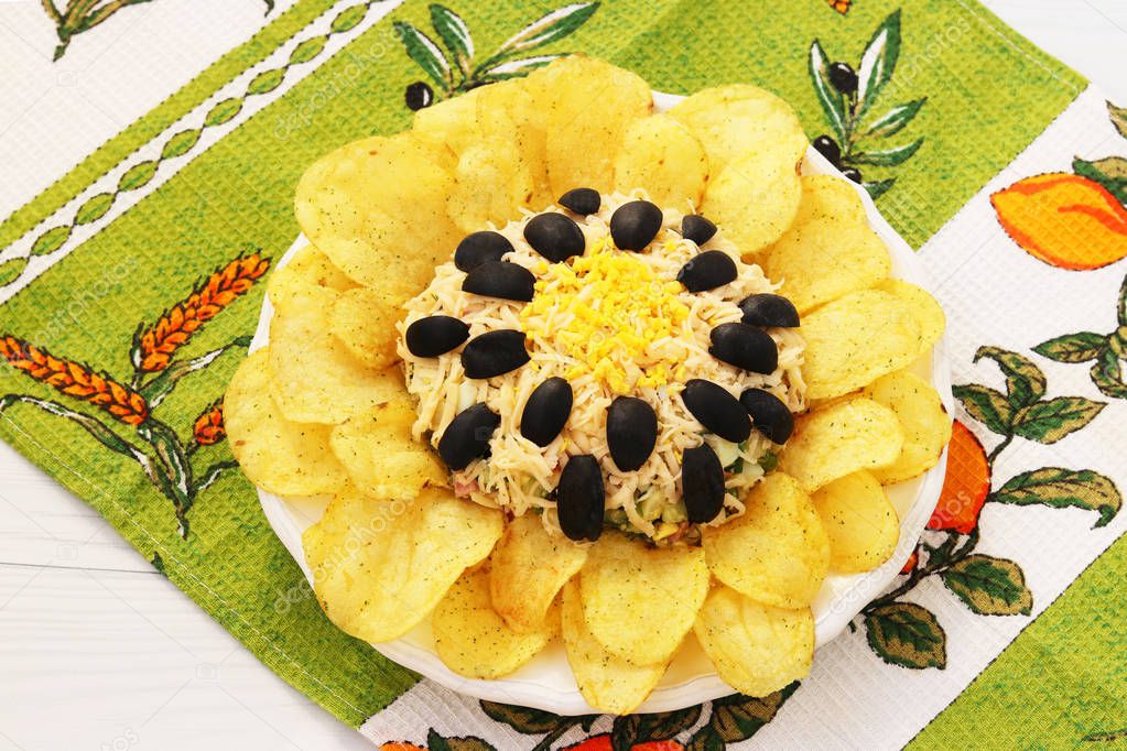 Salad in the form of sunflower, decorated with potato chips located on a plate